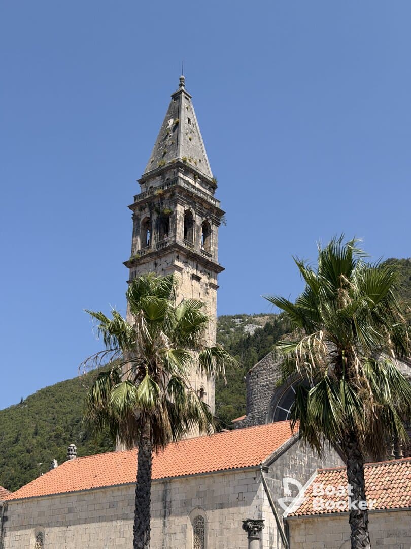 A view of a historic building with a tall tower and palm trees in the foreground, set against a clear blue sky. The architectural details suggest a rich history, making it a potential landmark for visitors.