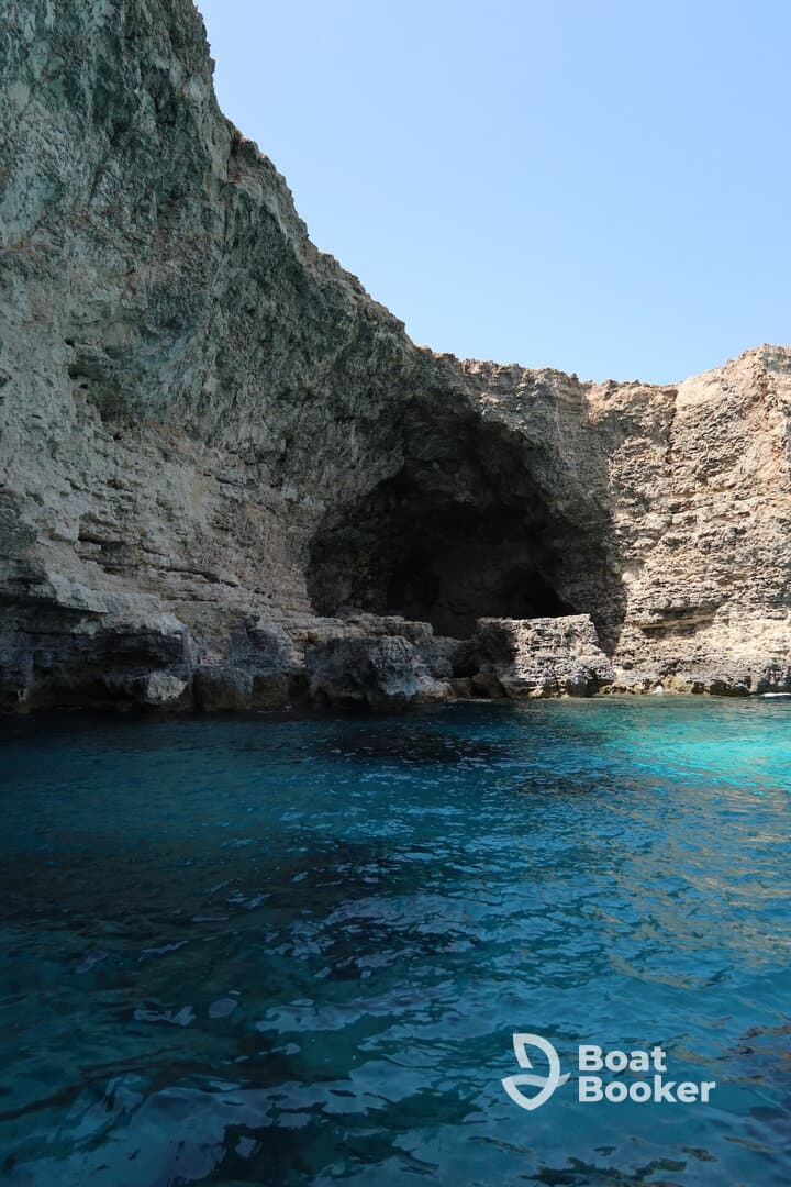 A stunning view of a rocky coastline with a cave entrance, surrounded by crystal-clear turquoise waters — an ideal spot for exploration and adventure.