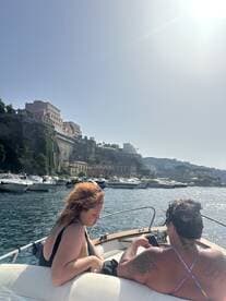A couple enjoys a relaxing moment on a boat, surrounded by scenic coastal views and other vessels, perfect for a day out on the water.