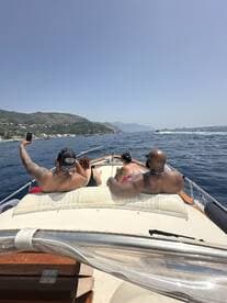 A group of friends enjoys a sunny day on the water, capturing memories aboard a boat with stunning coastal views in the background.