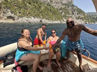 A lively group enjoys cocktails on a boat, celebrating together against a stunning coastal backdrop — perfect for memorable summer outings.