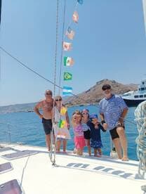 A joyful family poses together on a sailboat, surrounded by beautiful scenery and colorful flags, capturing a memorable sailing experience.