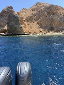 A clear view of the boat's outboard motors with a rugged rocky coastline in the background, showcasing the beauty of the surrounding waters.