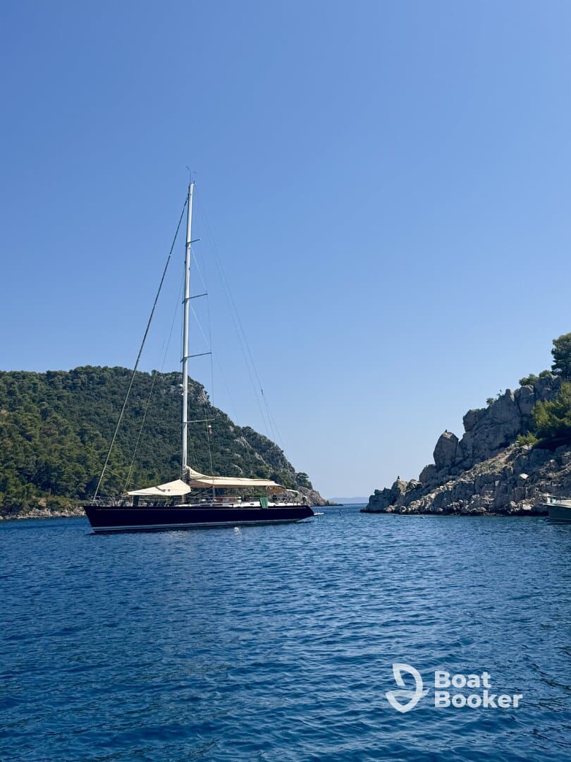 A stunning sailboat glides through calm waters, framed by lush green hills and rocky cliffs, perfect for scenic sailing adventures.