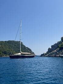 A stunning sailboat glides through calm waters, framed by lush green hills and rocky cliffs, perfect for scenic sailing adventures.