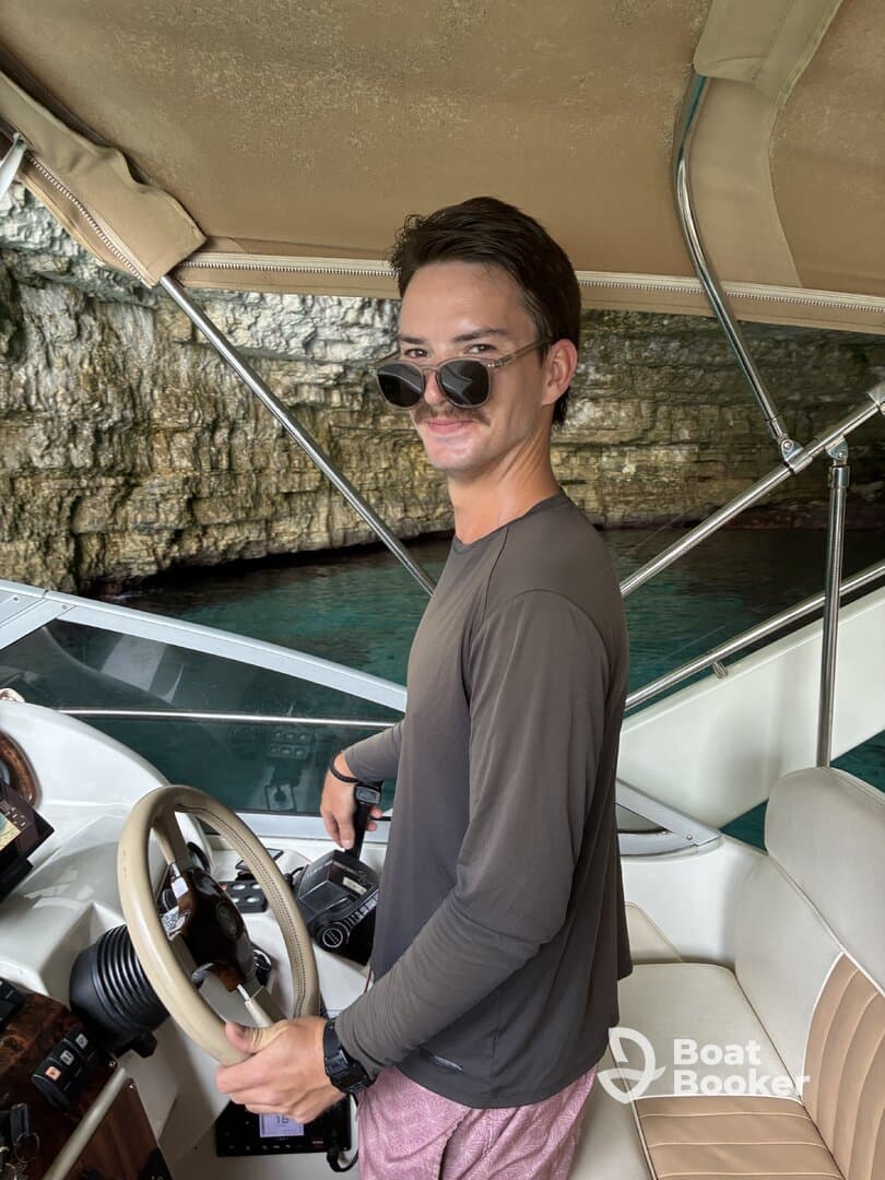 A young man confidently navigates the helm of a boat, showcasing the stylish interior and control console, perfect for a day on the water.