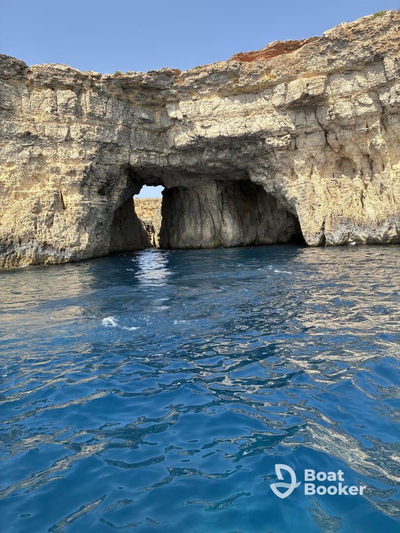 A stunning view of a natural rock formation with a cave opening, set against the vibrant blue waters — perfect for exploring coastal wonders.