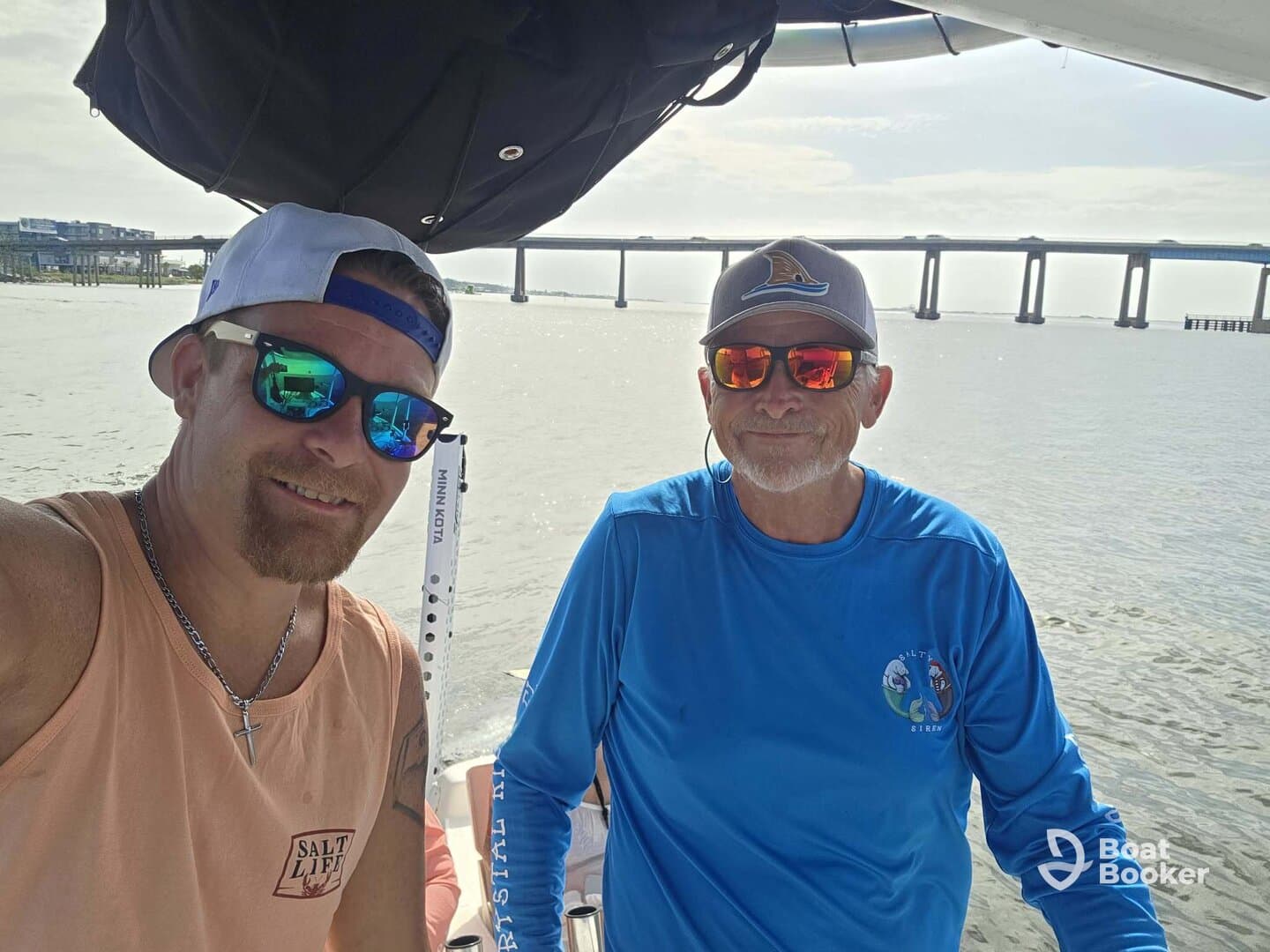 Two men enjoy a sunny day on the water, capturing a moment aboard their boat with a scenic backdrop of a bridge. Perfect for showcasing camaraderie and boating adventures.