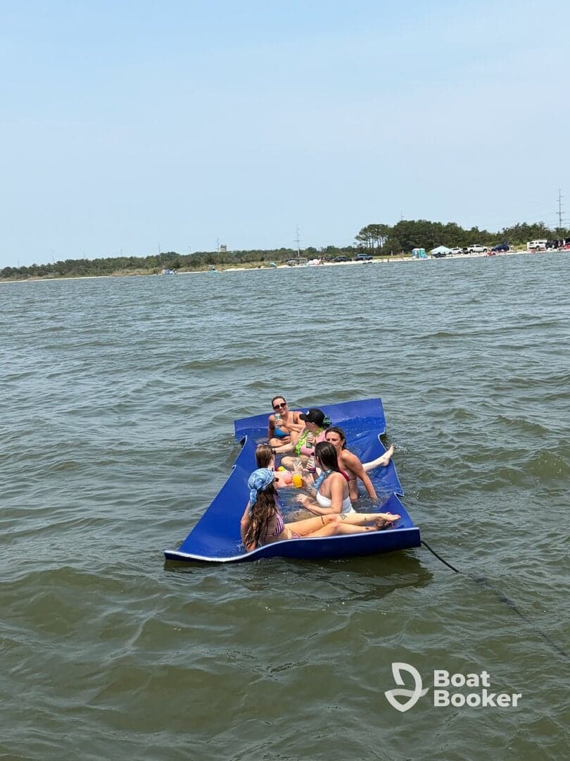 A lively group enjoys a day on a floating mat, sipping drinks and soaking up the sun — a perfect summer party on the water.