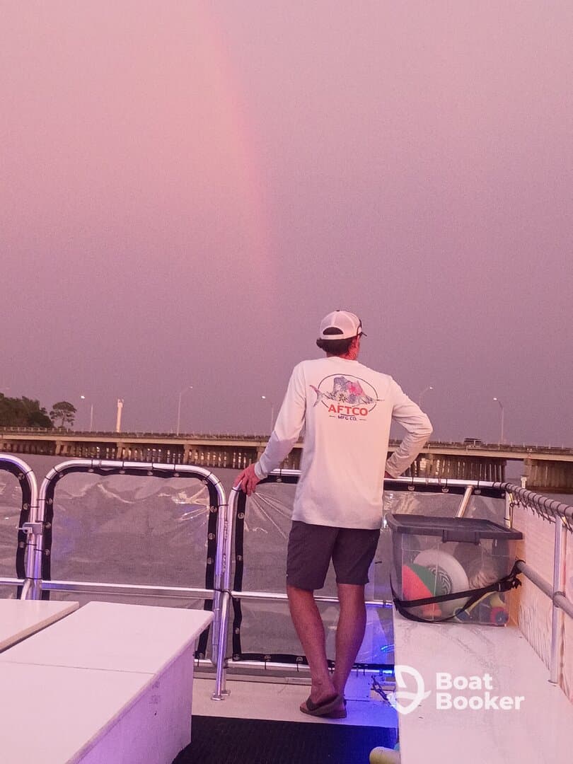 A person enjoys a serene moment on a boat, gazing at a beautiful rainbow against a twilight sky — a perfect backdrop for memorable boating experiences.