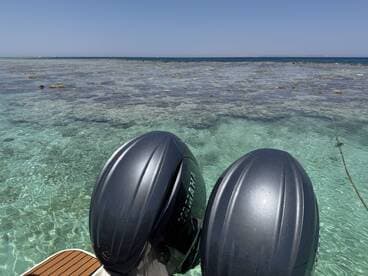 A close-up view of outboard motors on a boat, with a stunning backdrop of clear turquoise waters and coral formations, ideal for exploring marine life.