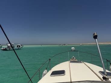 A scenic view from the bow of a boat navigating through turquoise waters, showcasing a tranquil marine environment with other vessels in the background.