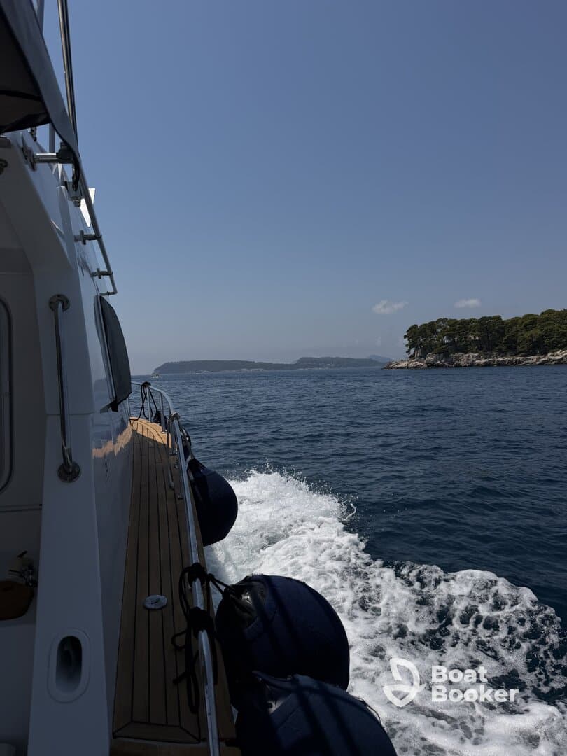 A side view of a boat cruising through calm waters, showcasing the vessel's sleek design and the beautiful coastal scenery in the background.