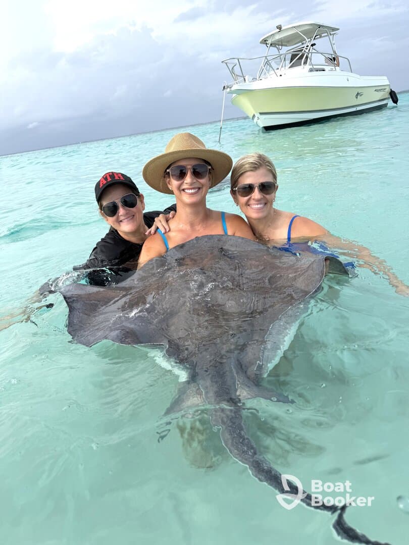 Three women interact with a stingray in shallow turquoise waters, creating a memorable wildlife experience in a tropical paradise.