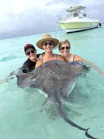Three women interact with a stingray in shallow turquoise waters, creating a memorable wildlife experience in a tropical paradise.