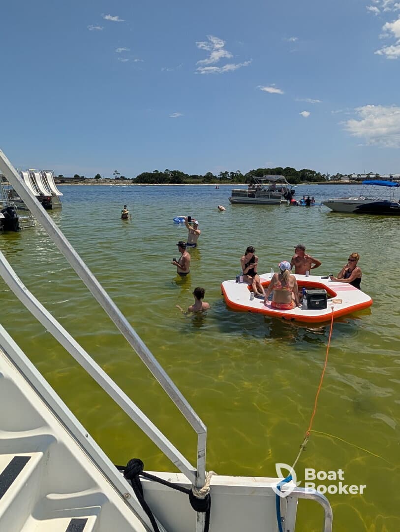 A lively group enjoys a fun day at the sandbar, swimming and relaxing on a floating platform — the perfect setting for summer parties on the water.