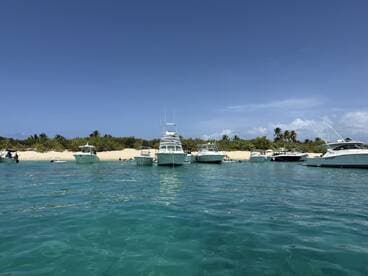 A vibrant scene at a sandbar with multiple boats anchored, showcasing a perfect day for swimming and relaxation on the beach.
