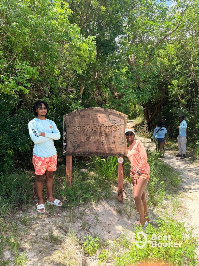 A group poses by the Preacher's Cave sign, capturing a moment of adventure and exploration in a lush tropical setting.