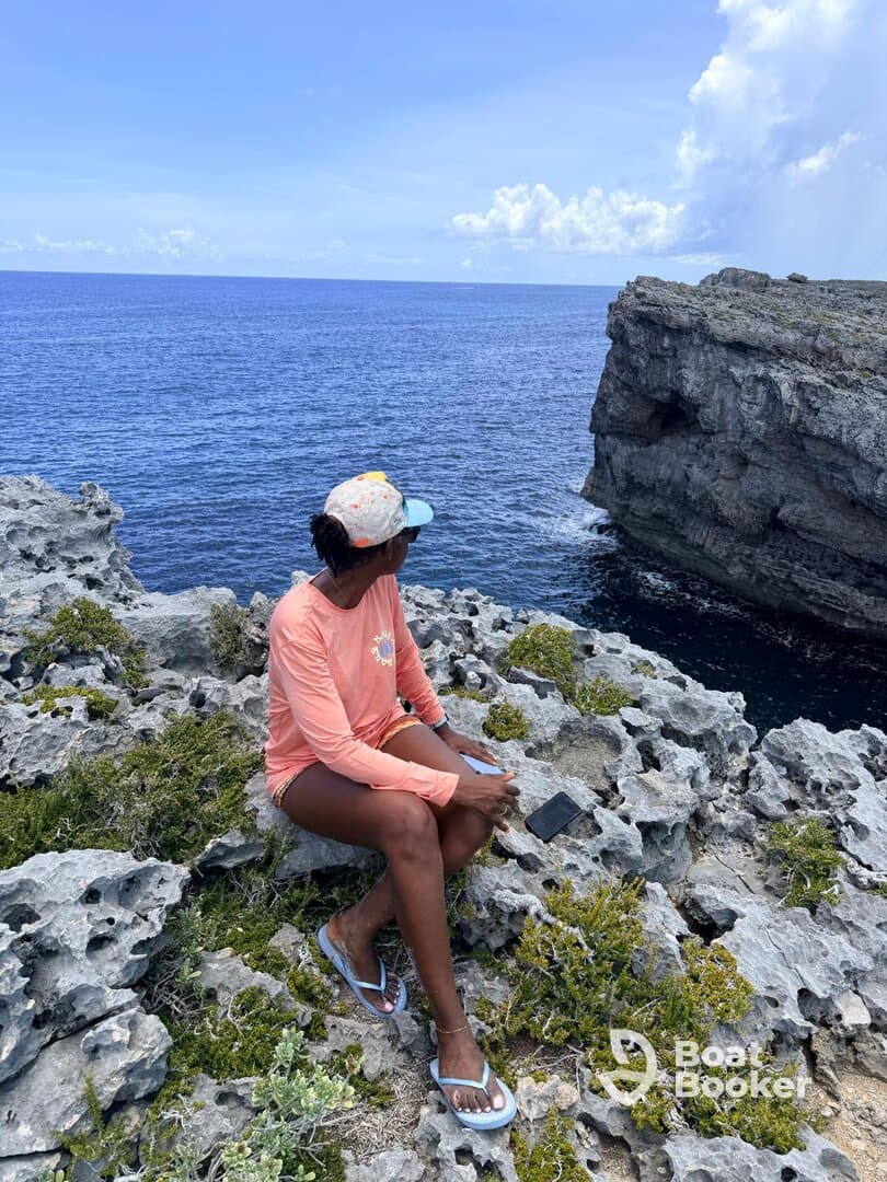 A woman enjoys the stunning ocean view from a rocky coastline, capturing the essence of relaxation and natural beauty during her boating adventure.