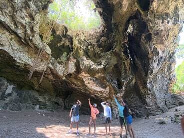 A group of friends explores a stunning cave, pointing at the unique rock formations above — a perfect adventure in nature.