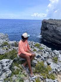 A woman enjoys the stunning ocean view from a rocky coastline, capturing the essence of relaxation and natural beauty during her boating adventure.