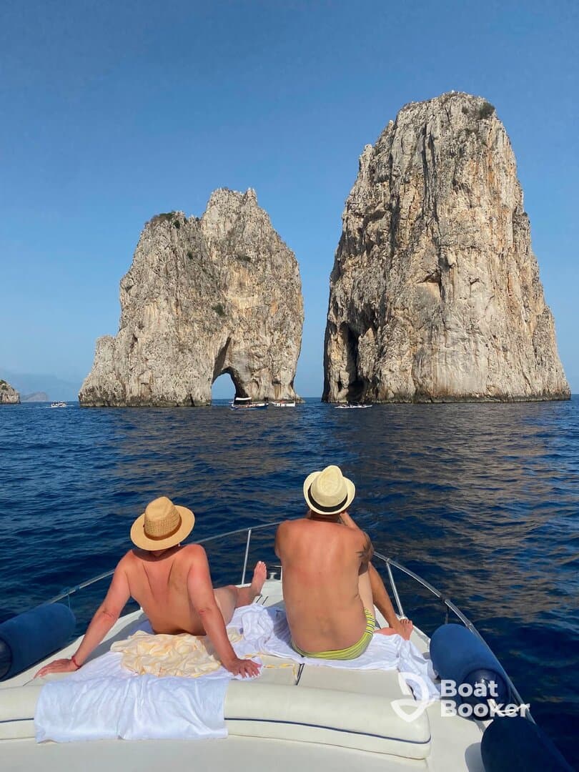Two friends relax on the bow of a boat, enjoying the stunning view of the iconic rock formations of Capri — a perfect moment for sightseeing and adventure on the water.