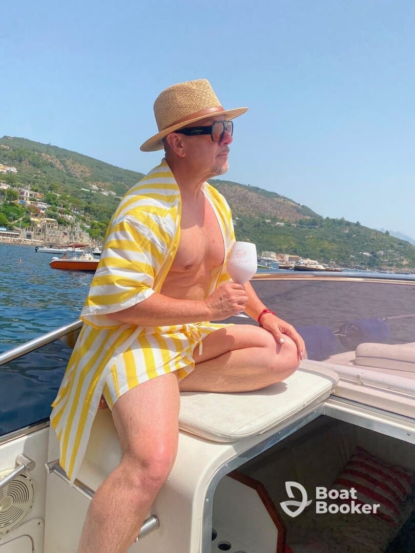 A man enjoys a refreshing cocktail while relaxing on the deck of a boat, soaking up the sun and picturesque views — perfect for a summer getaway.