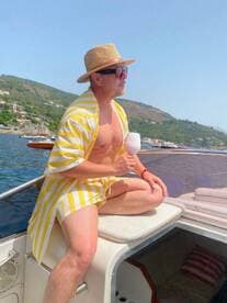 A man enjoys a refreshing cocktail while relaxing on the deck of a boat, soaking up the sun and picturesque views — perfect for a summer getaway.