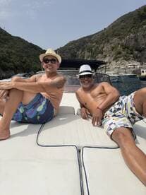Two friends relax and enjoy the sun on the deck of a boat, surrounded by stunning coastal scenery — a perfect moment for leisure and camaraderie on the water.