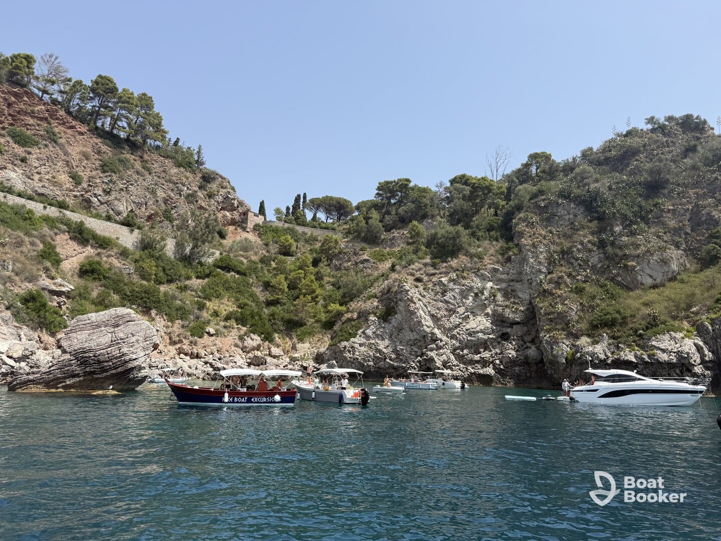A picturesque scene featuring multiple boats anchored in a serene cove, surrounded by lush greenery and rocky cliffs — perfect for a day of exploration and relaxation on the water.