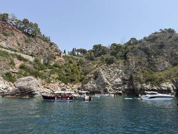 A picturesque scene featuring multiple boats anchored in a serene cove, surrounded by lush greenery and rocky cliffs — perfect for a day of exploration and relaxation on the water.