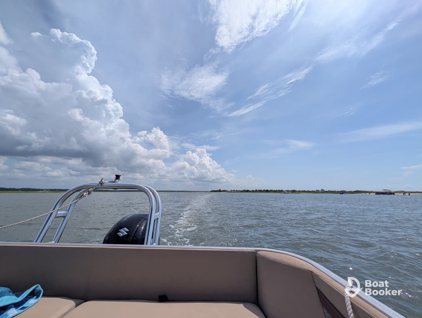 A scenic view from the back of a pontoon boat cruising through calm waters, showcasing the beautiful sky and distant shoreline.