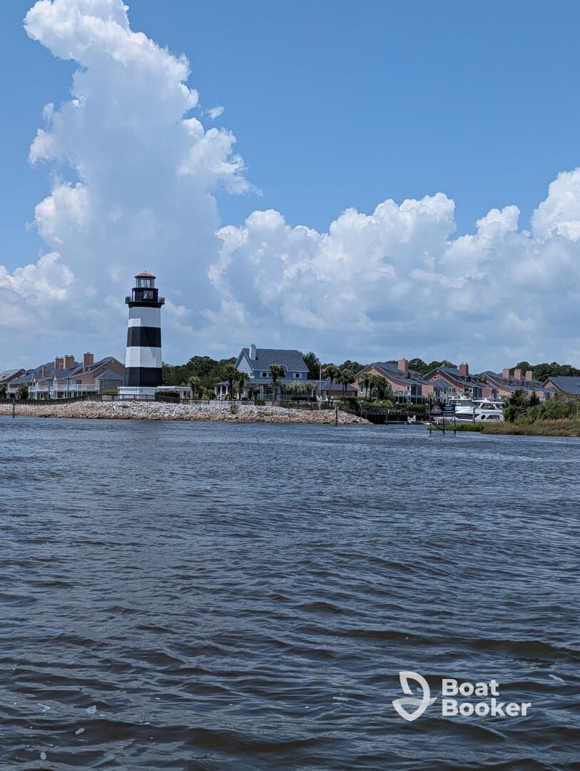 A picturesque view of a black and white lighthouse against a backdrop of fluffy clouds and coastal homes, perfect for capturing the charm of waterfront destinations.