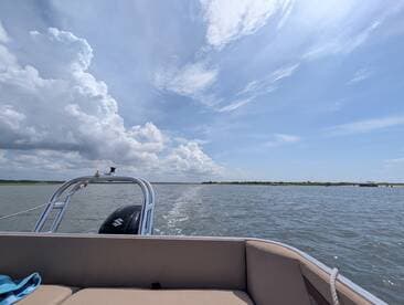 A scenic view from the back of a pontoon boat cruising through calm waters, showcasing the beautiful sky and distant shoreline.
