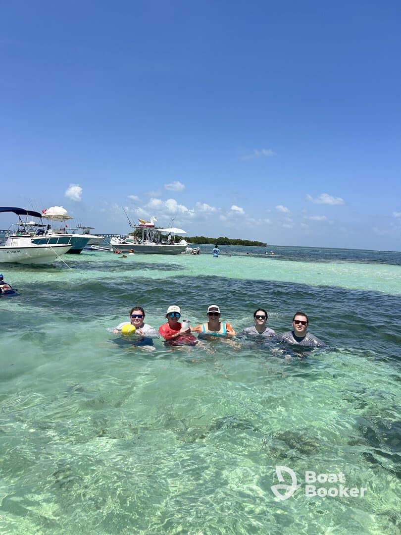 A lively group enjoys a sandbar stop, swimming in crystal-clear waters while surrounded by boats — a perfect day for fun and relaxation on the water.