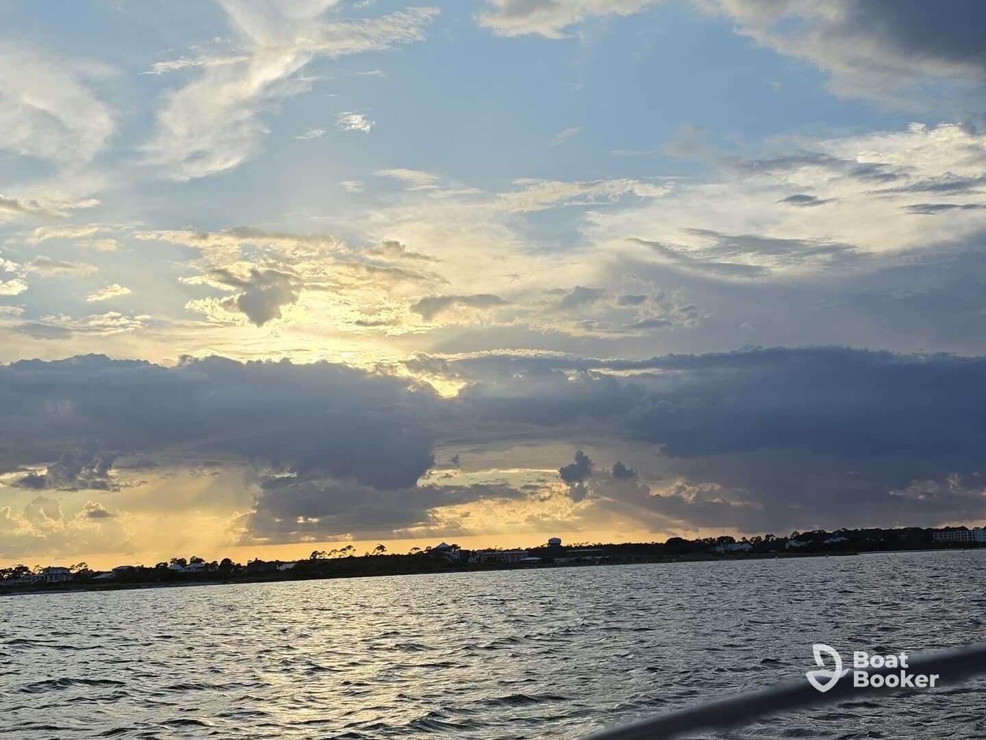 A stunning sunset casts golden hues over the water, creating a picturesque backdrop of the coastline — perfect for capturing the beauty of a tranquil evening on the water.