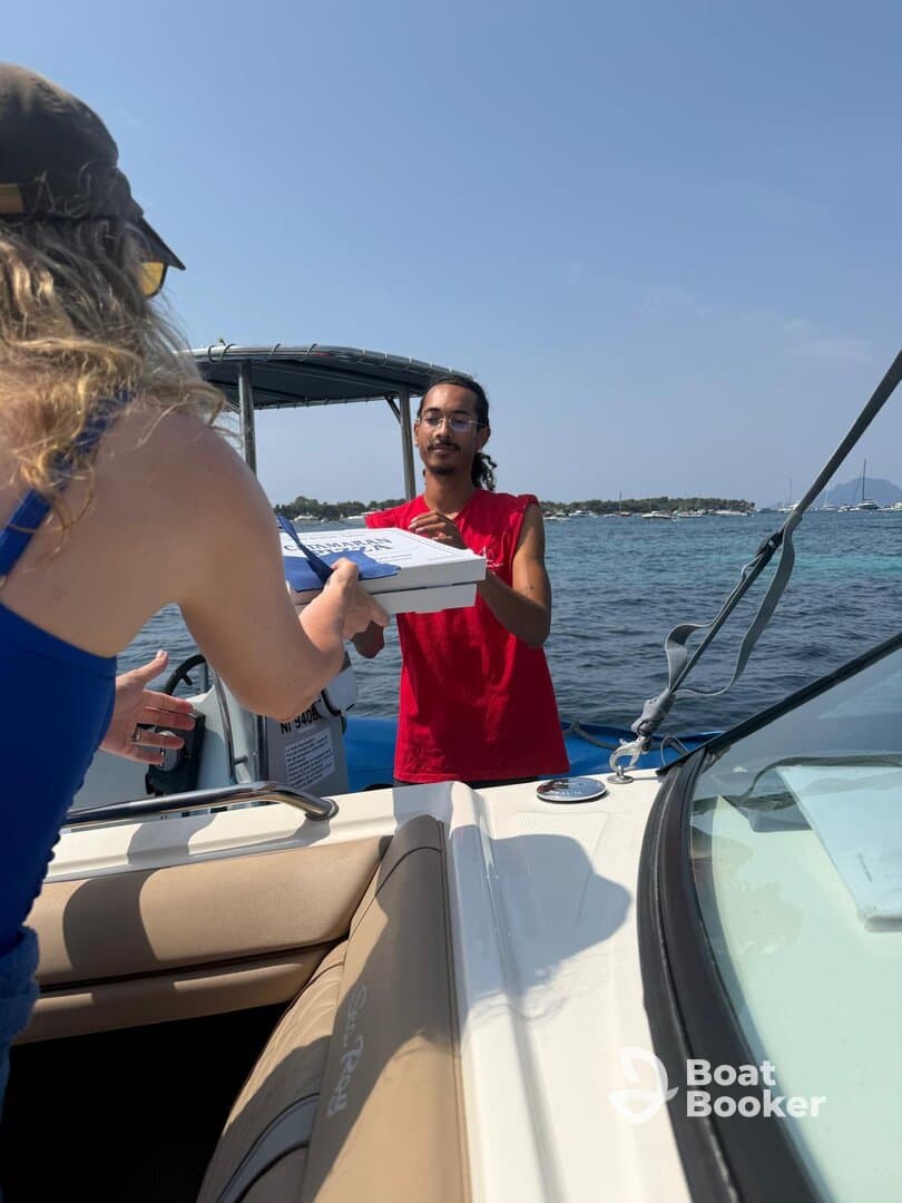A woman hands over a pizza box to a man on a boat, capturing a fun food delivery experience on the water — perfect for enjoying meals while cruising.