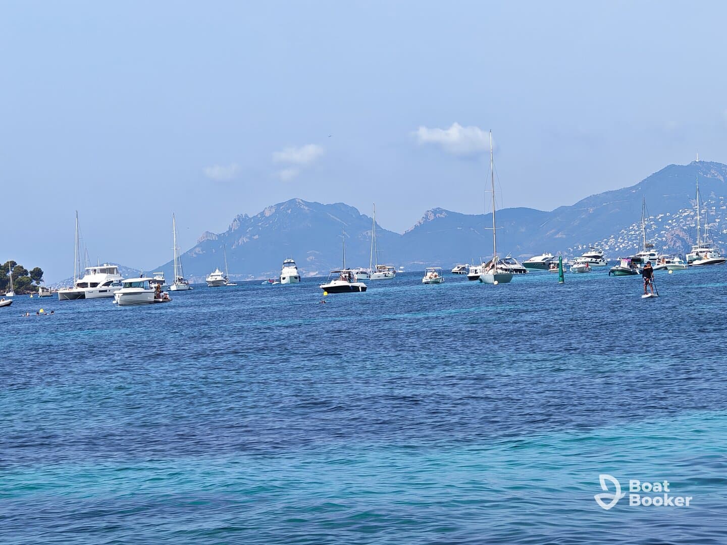A vibrant scene of various boats and a paddleboarder enjoying the clear waters, showcasing the beauty of a coastal getaway.