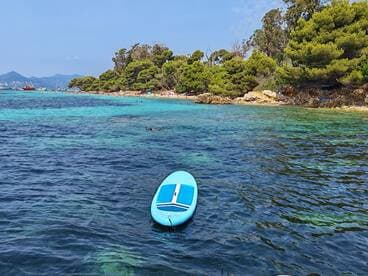 A vibrant scene showcasing a paddleboard in clear waters, with beachgoers enjoying the sun and swimming in the background — perfect for a day of relaxation and adventure.
