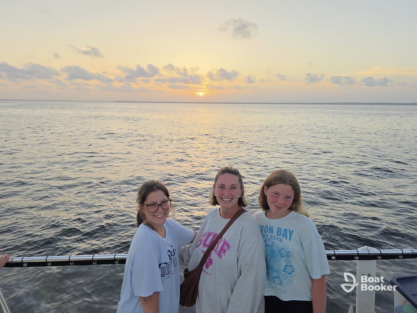 A joyful group of three poses for a photo against a stunning sunset backdrop while enjoying their time on the water — perfect for family outings or sunset cruises.