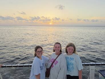A joyful group of three poses for a photo against a stunning sunset backdrop while enjoying their time on the water — perfect for family outings or sunset cruises.