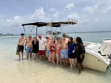 A cheerful group of friends enjoys a day at the beach, posing by their boat in shallow waters — a perfect moment of summer fun and adventure.