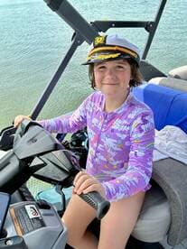A cheerful child dressed in a colorful captain's outfit sits at the helm of a boat, ready for adventure on the water.