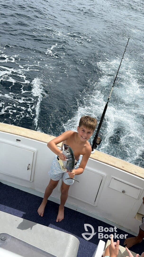 A young boy proudly holds up his catch while fishing on a boat, showcasing the joy of a successful day on the water.