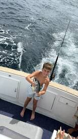 A young boy proudly holds up his catch while fishing on a boat, showcasing the joy of a successful day on the water.