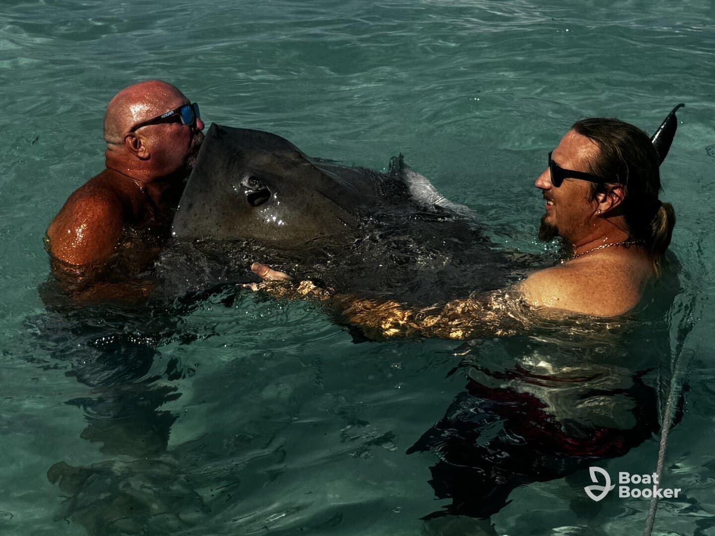 Two men engage in a close encounter with a stingray in shallow waters, showcasing an unforgettable wildlife experience.
