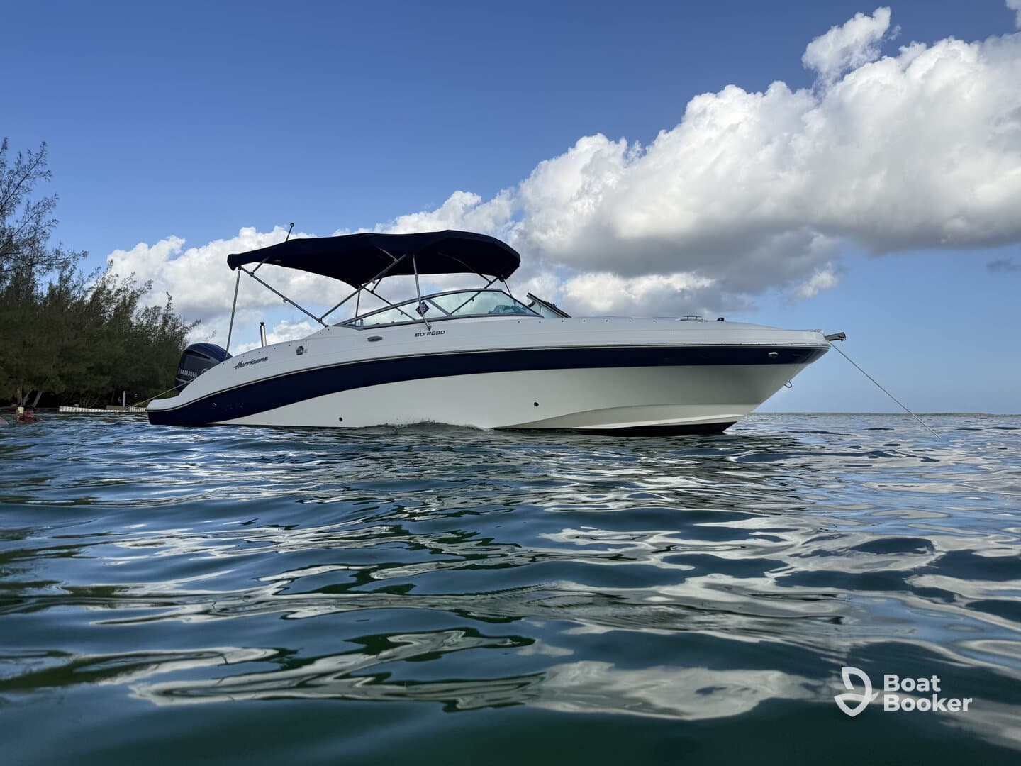 A sleek speedboat is anchored in calm waters, showcasing its elegant design against a backdrop of blue skies and fluffy clouds — perfect for a day on the water.