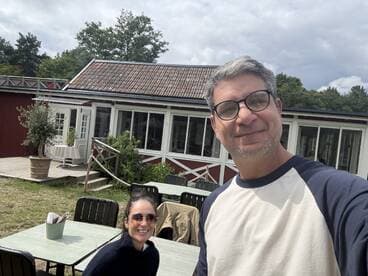 A couple poses for a selfie outside a building, capturing a casual moment in a scenic setting.