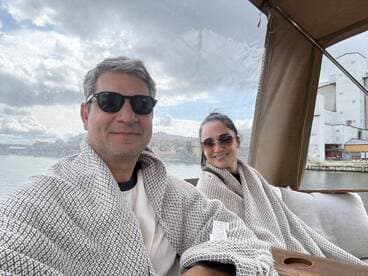 A couple enjoys a cozy moment on a boat, wrapped in blankets while taking in the scenic waterfront views — perfect for a relaxing day on the water.