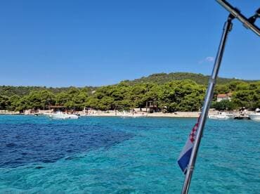 A picturesque view of a Croatian coastline with several boats anchored near a sandy beach, showcasing the beauty of summer outings on the water.